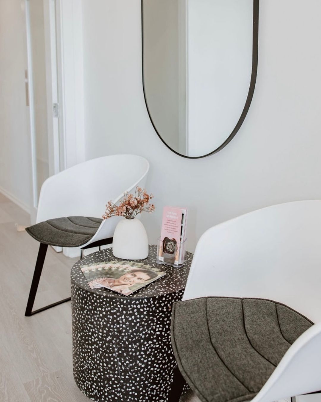 Two white chairs and marble side table with mirror on wall