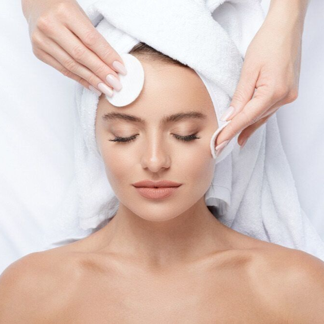 Beautician cleansing a woman’s face with cotton pads