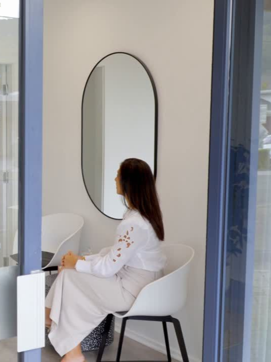 Woman sitting in white chair with mirror on wall
