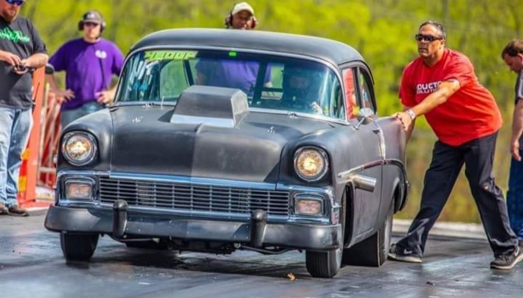 A group of men are pushing a black car on a race track.