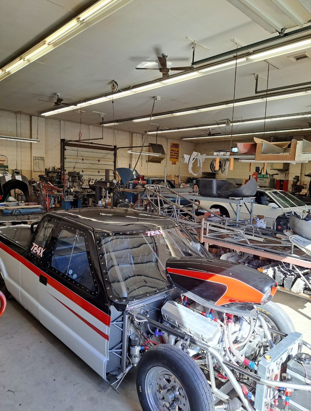 A car is parked in a garage with a motorcycle in the background.