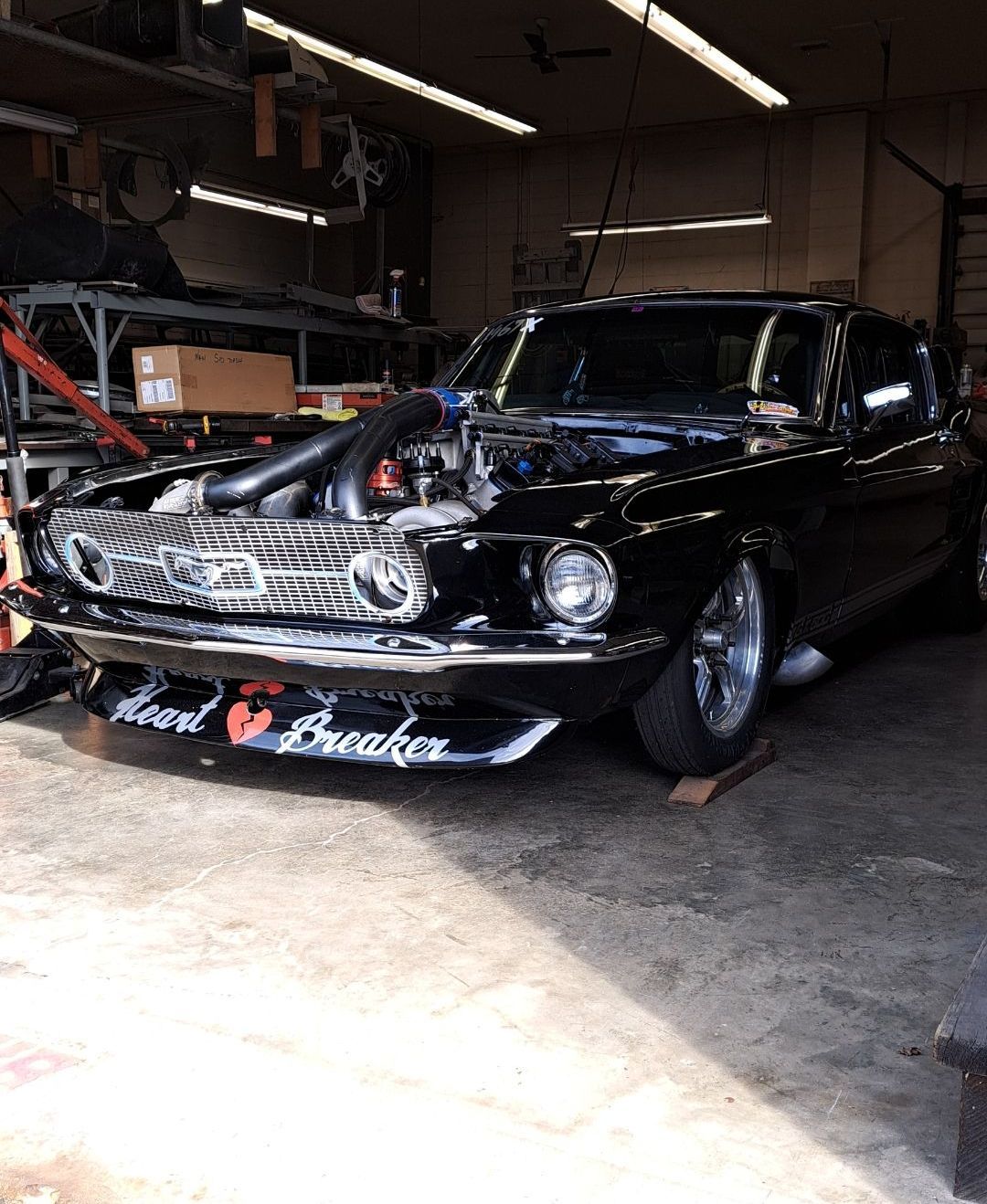 A black mustang is parked in a garage with the hood open