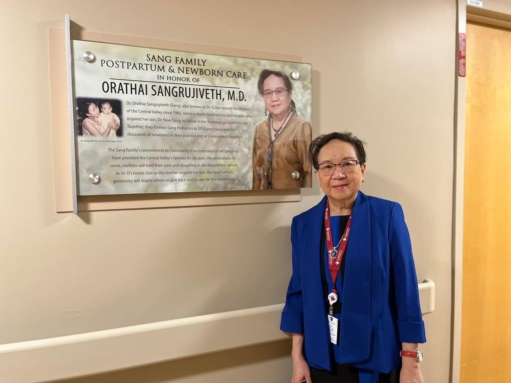 A woman in a blue jacket is standing in front of a plaque on a wall.