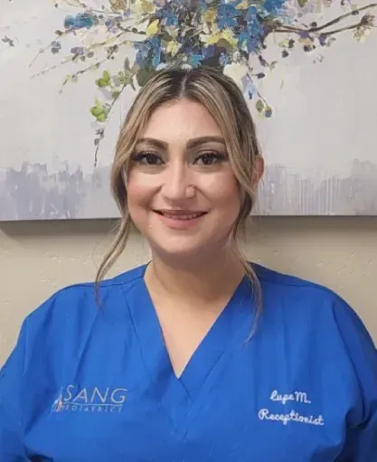 A woman in a blue scrub top is smiling in front of a painting.