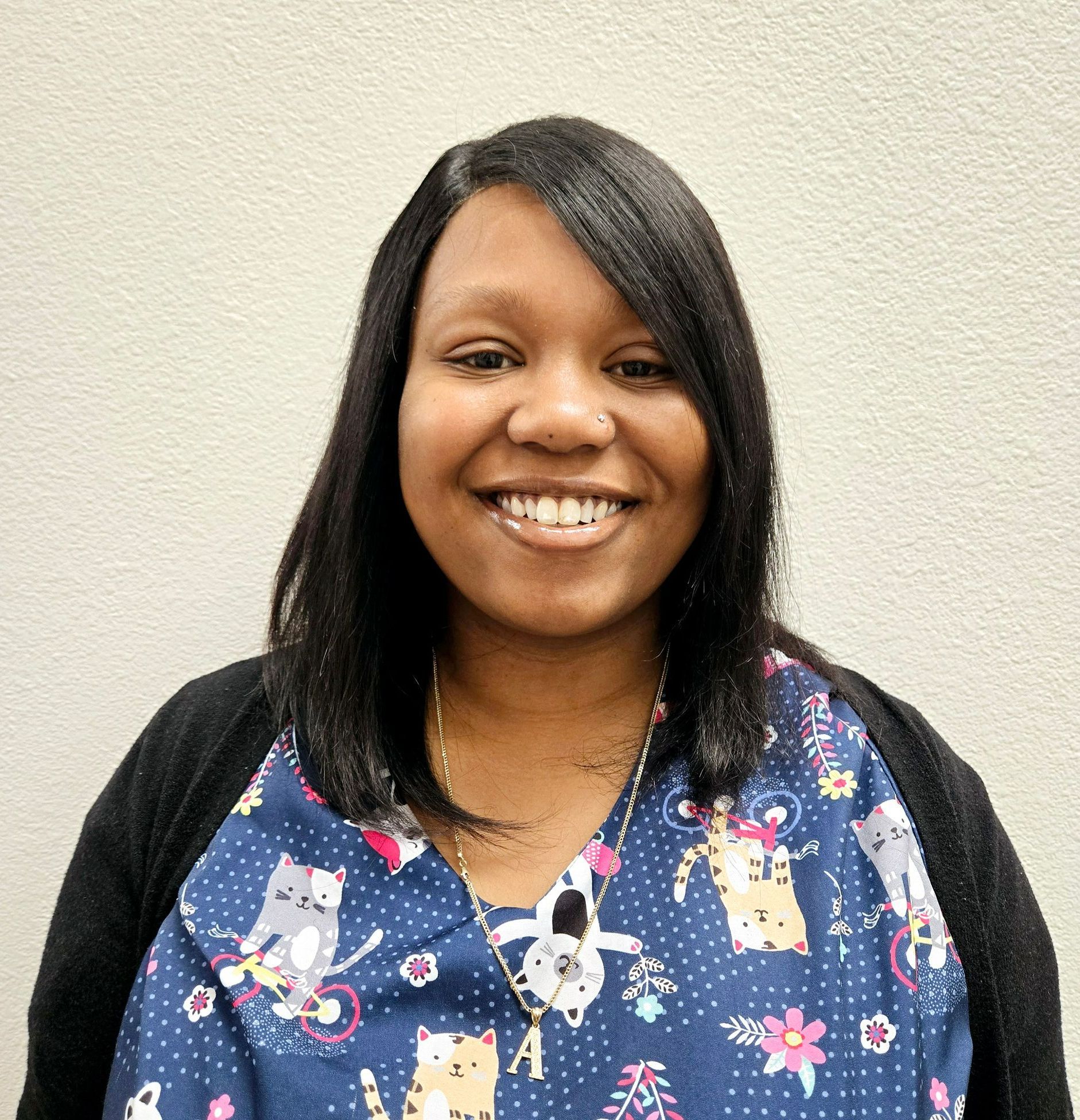 A woman wearing a scrub top with cats on it is smiling for the camera.