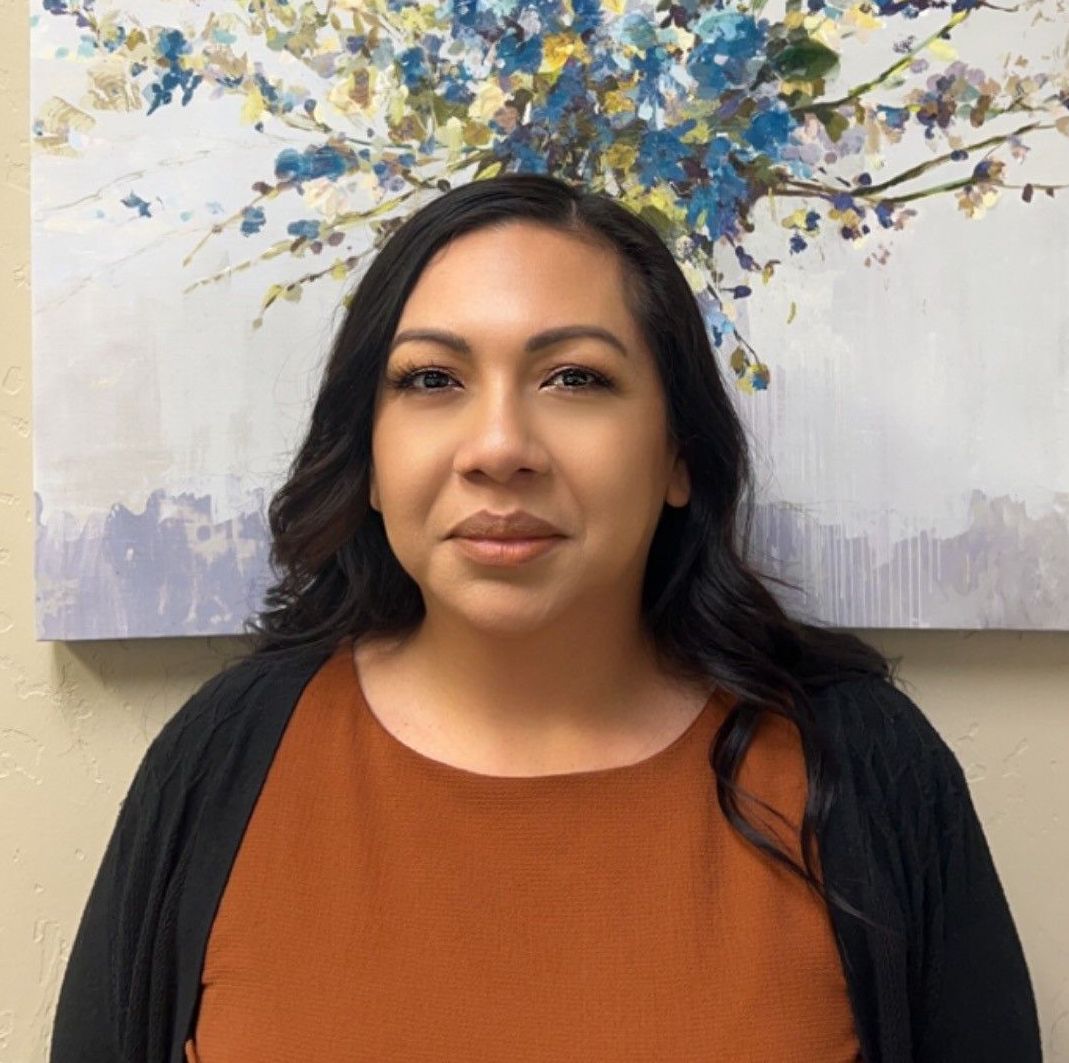 A woman is standing in front of a painting of flowers on a wall.