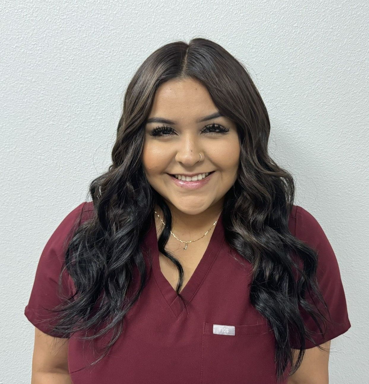 A woman in a maroon scrub top is smiling for the camera.