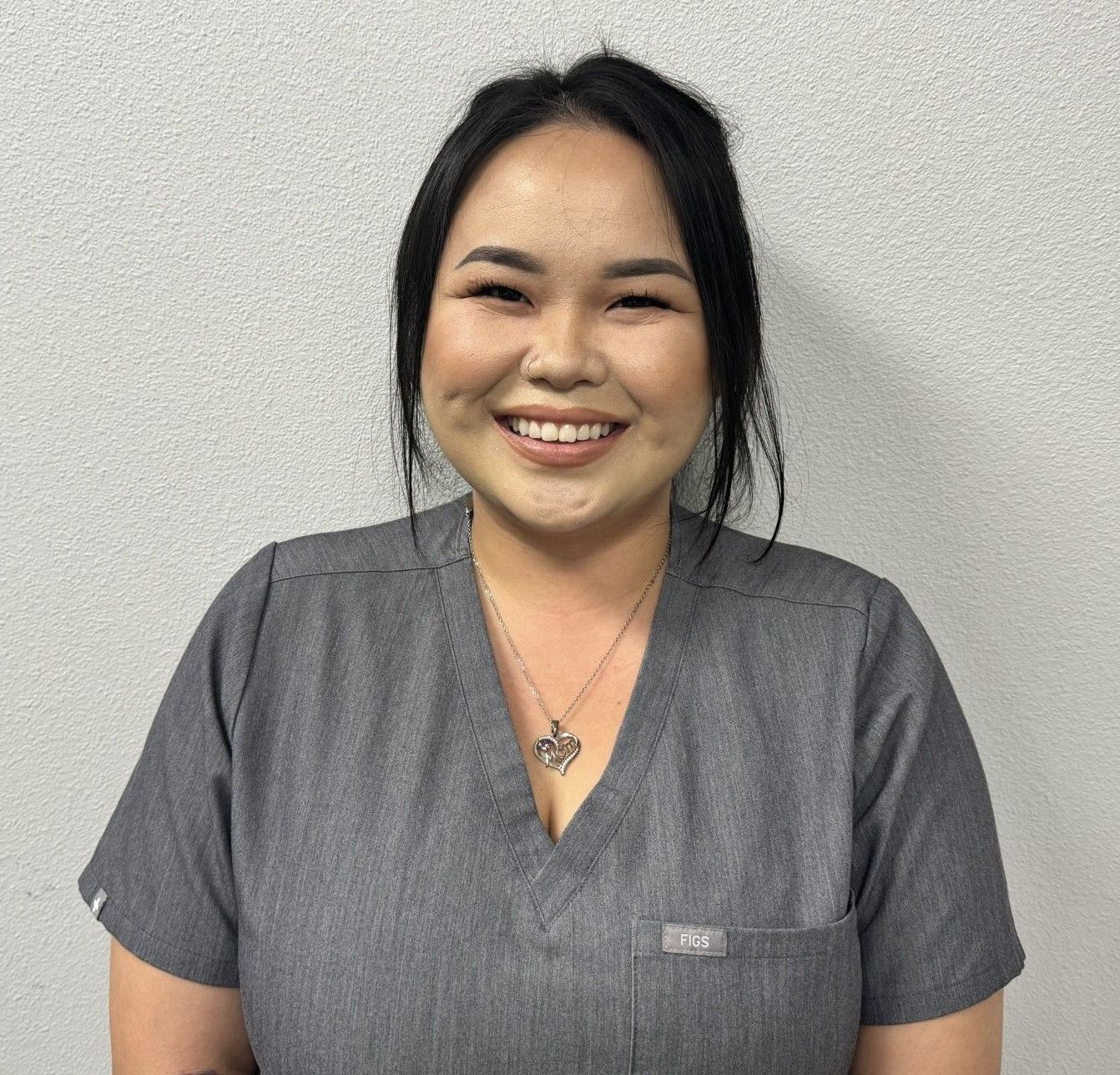 A woman in a gray scrub top is smiling for the camera.
