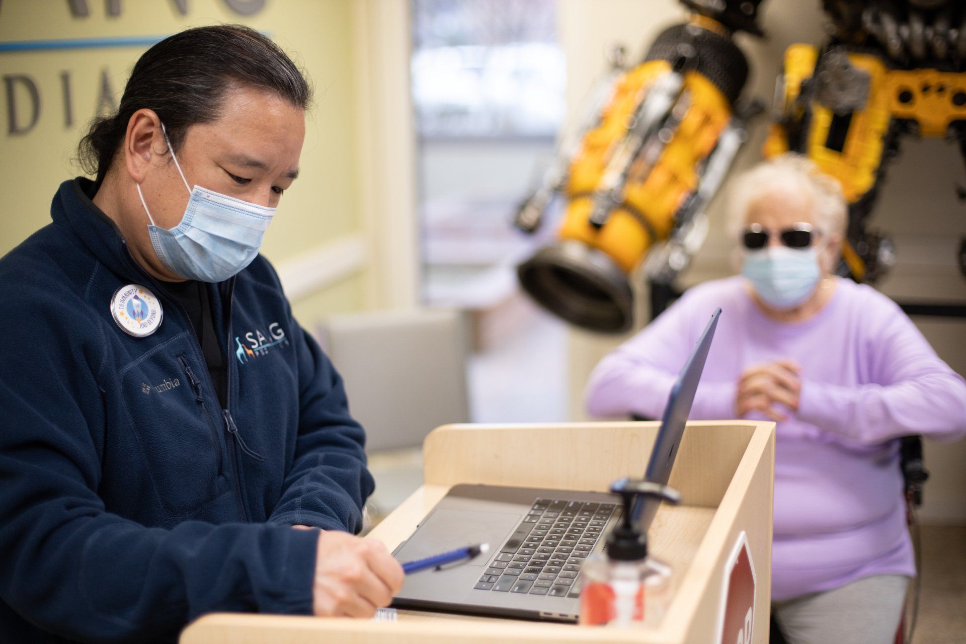 A man wearing a mask is sitting at a podium with a laptop.