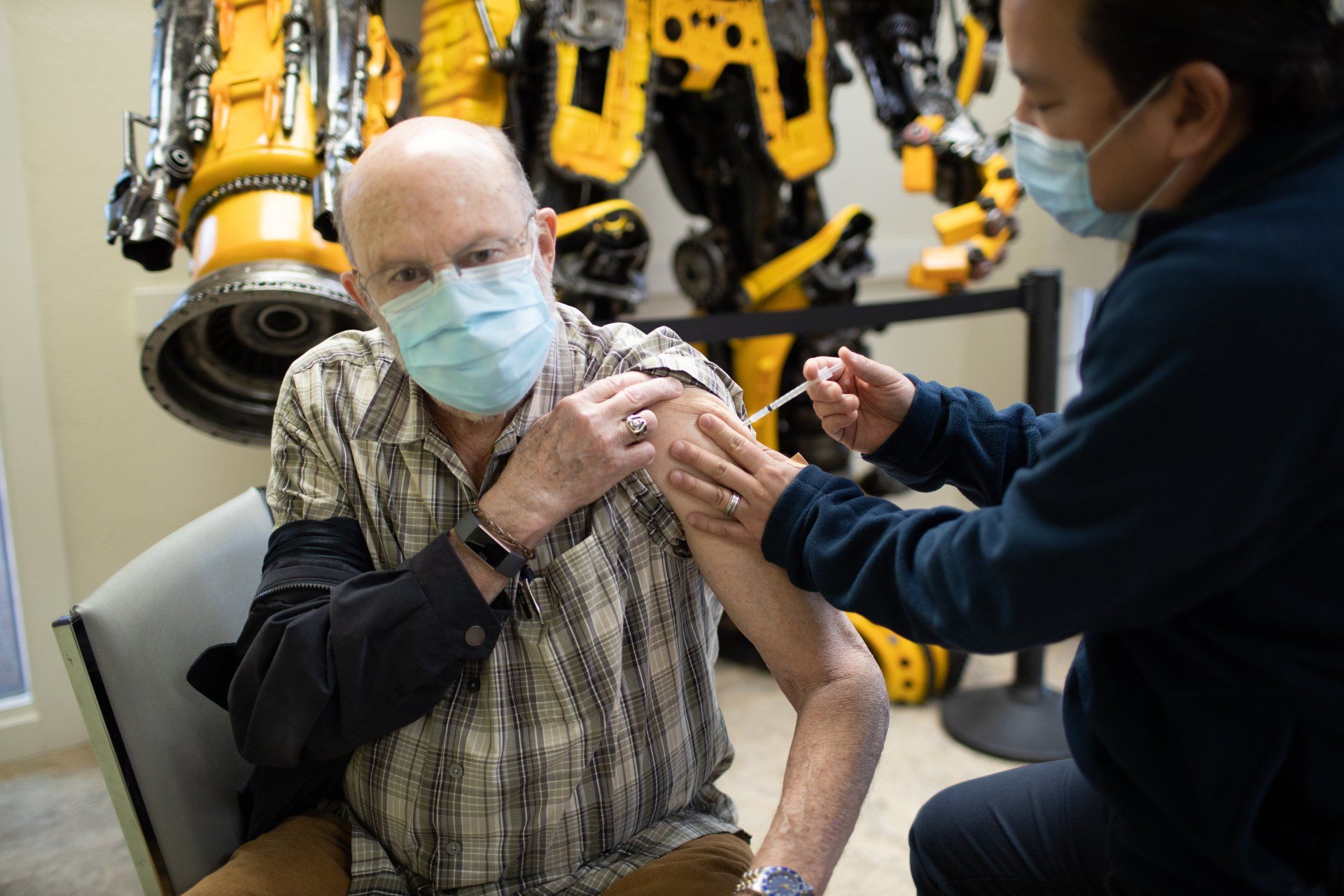 A man wearing a mask is getting a vaccine from a nurse.