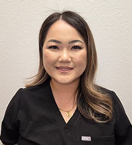 A woman in a black scrub top is smiling for the camera.