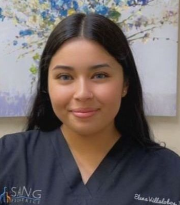 A woman in a black scrub top is standing in front of a painting.