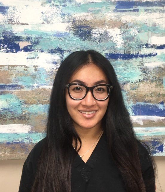 A woman wearing glasses and a black shirt is smiling in front of a painting.