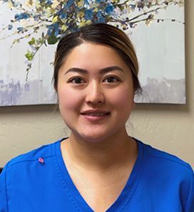 A woman in a blue scrub is smiling in front of a painting on the wall.