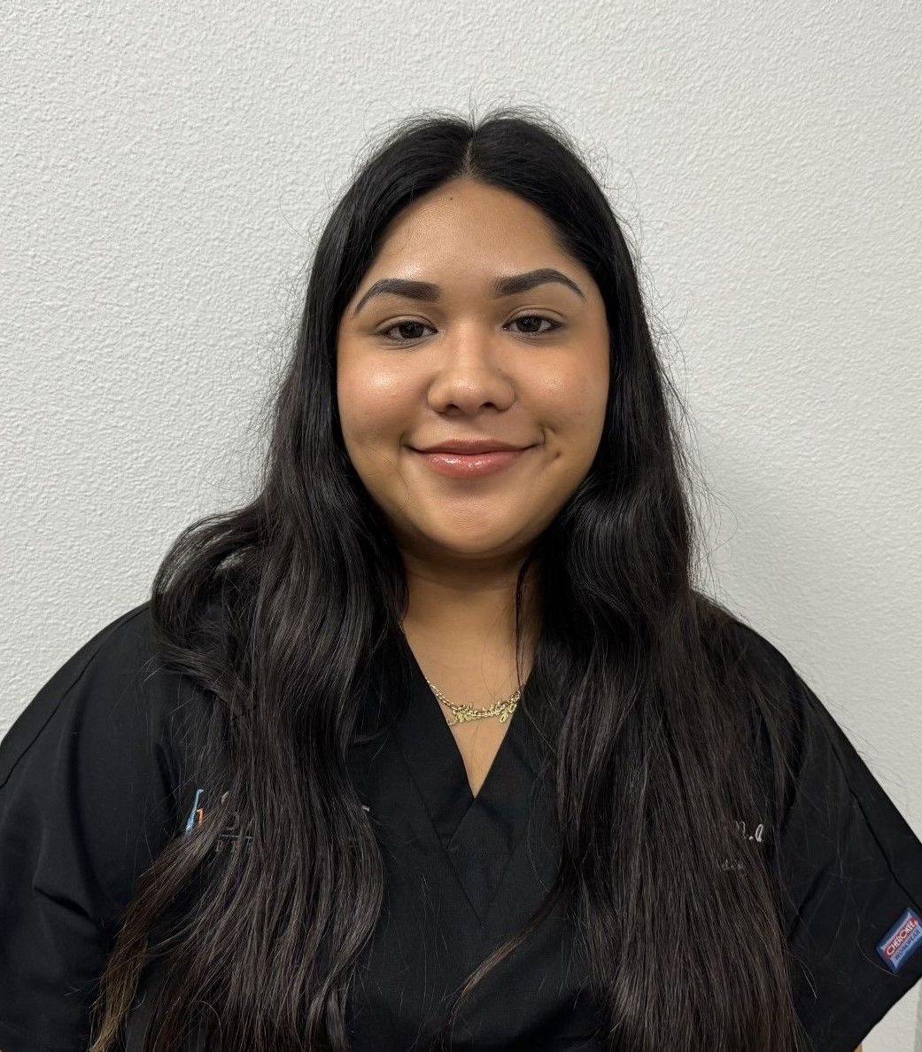 A woman with long hair is wearing a black scrub top and smiling for the camera.
