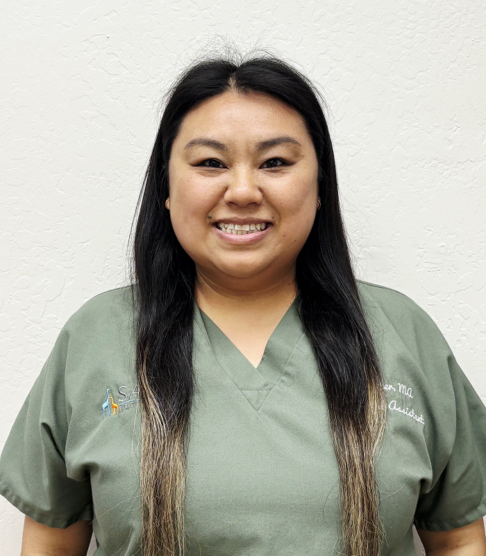 A woman wearing glasses and a blue scrub is standing in front of a painting.
