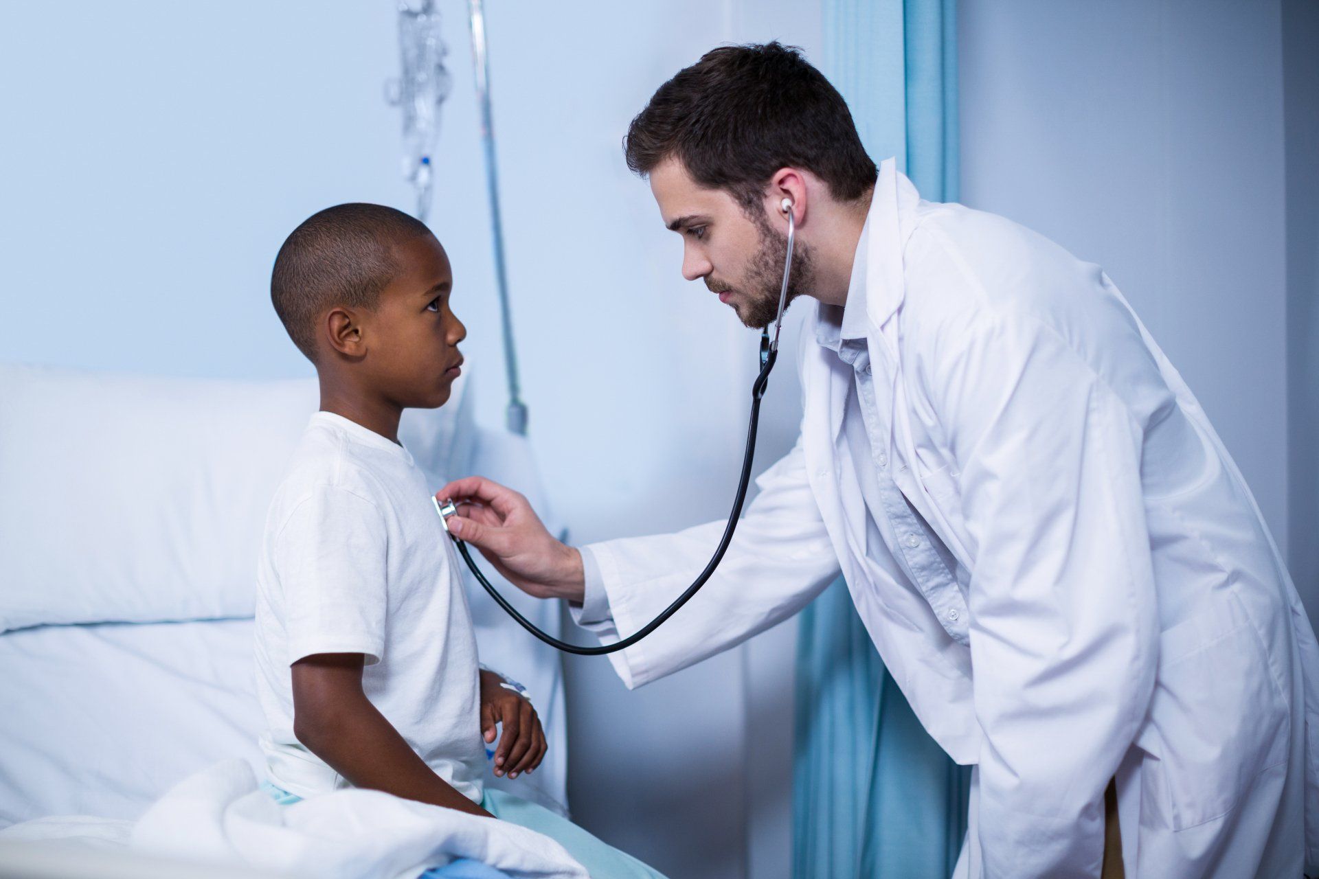A doctor is examining a young boy with a stethoscope in a hospital room.
