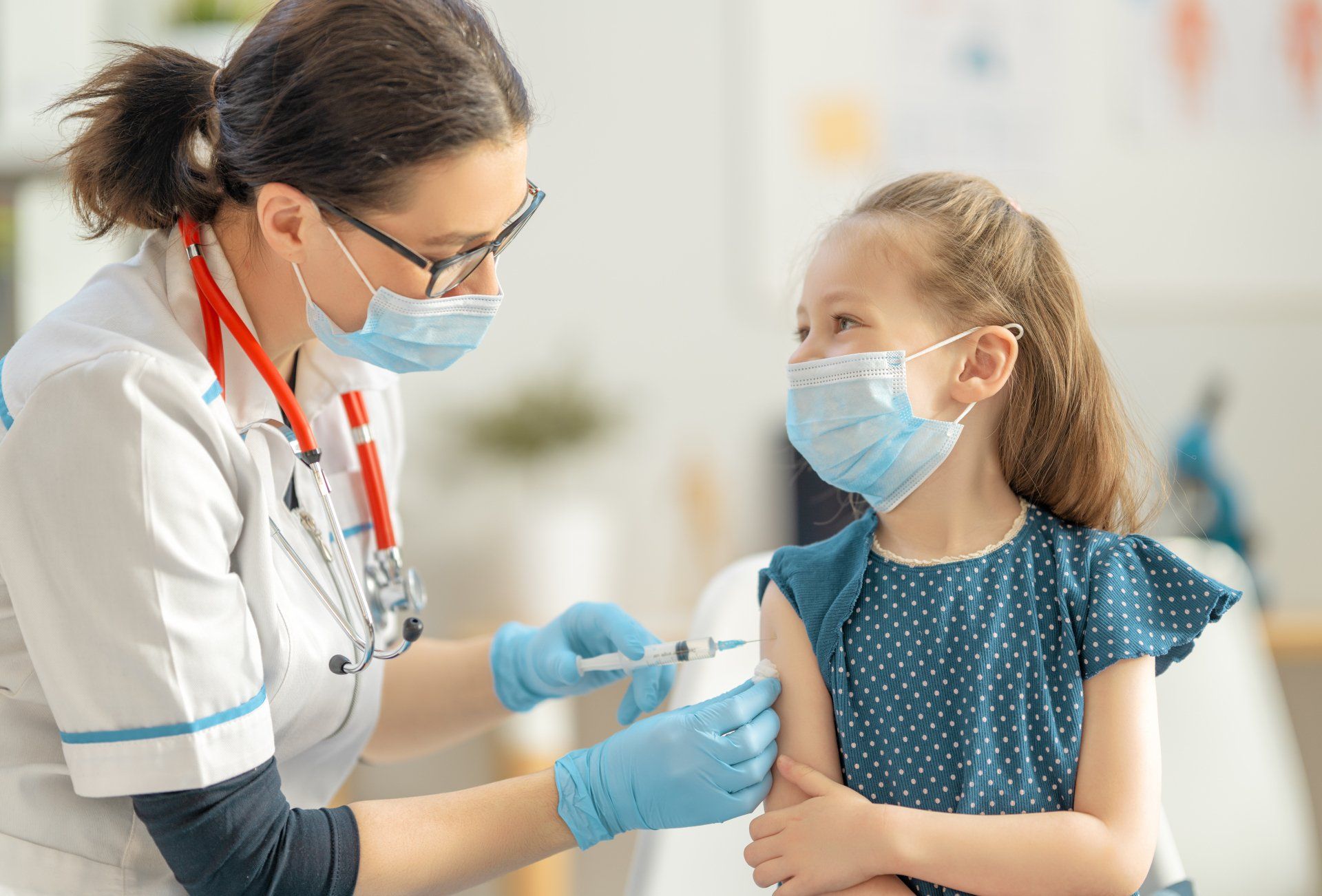 A little girl wearing a mask is getting a vaccine from a doctor.