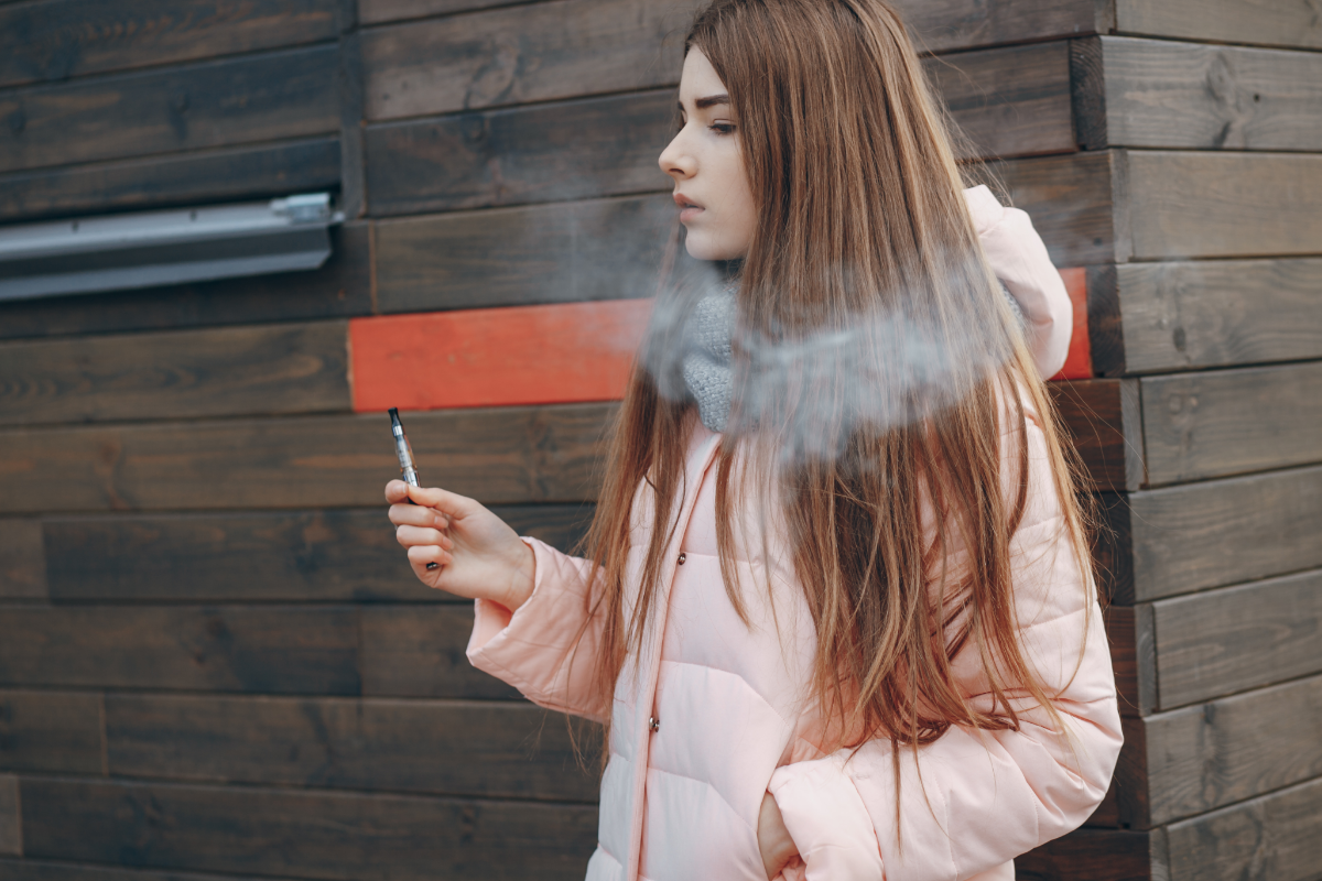 A teenage girl smoking and inhaling nicotine from an e-cigarette