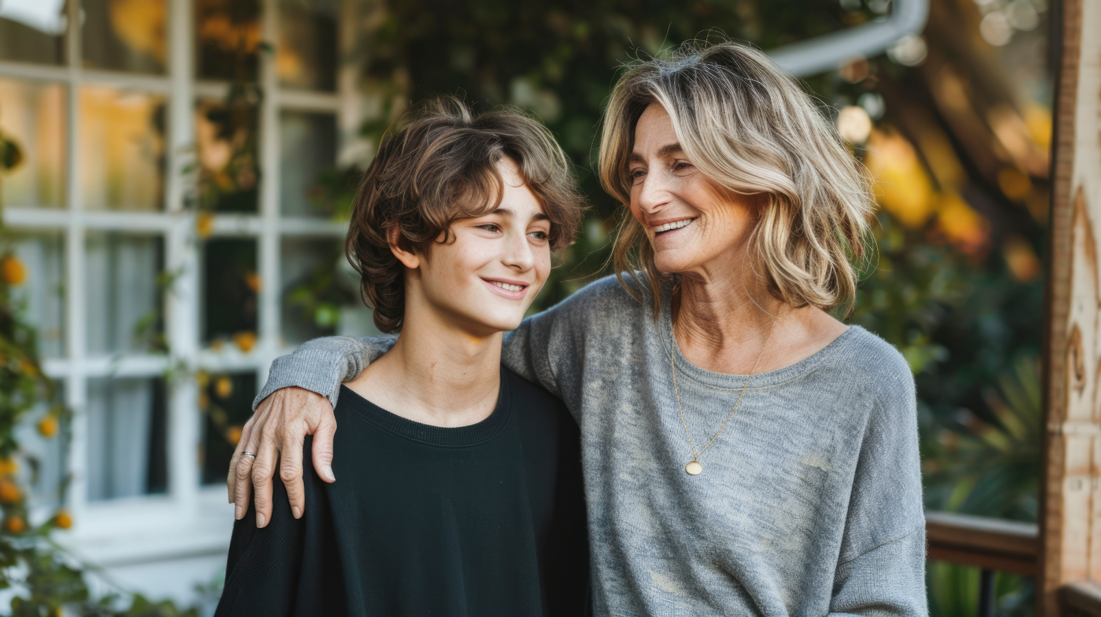 A woman and a boy are standing next to each other on a porch.