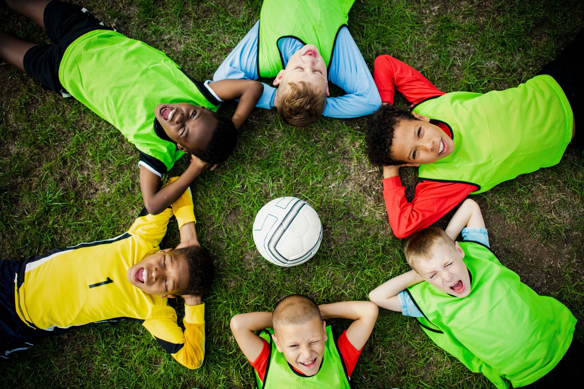 A group of young boys are laying in a circle with their heads on a soccer ball.