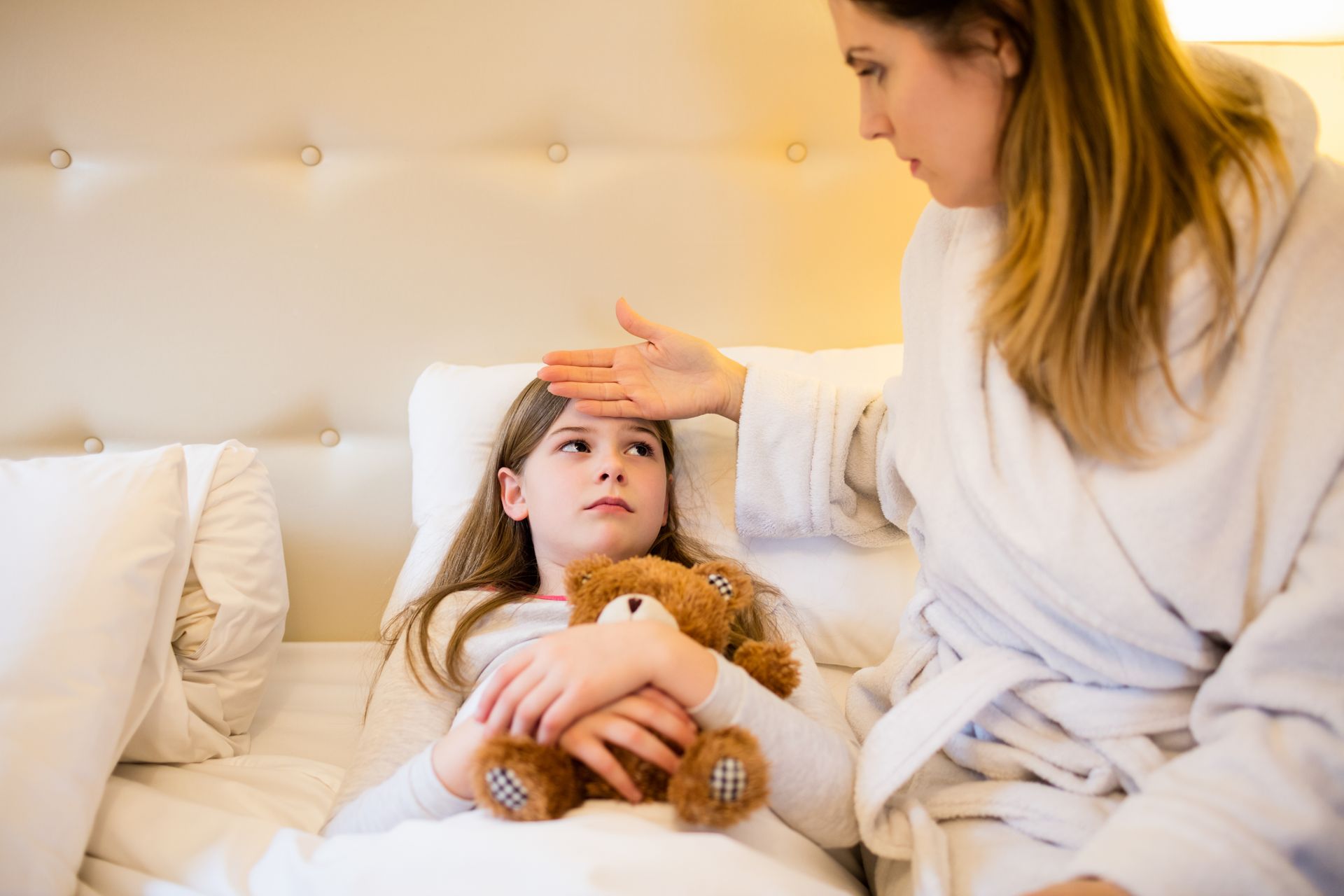 A woman is taking a child 's temperature in bed.