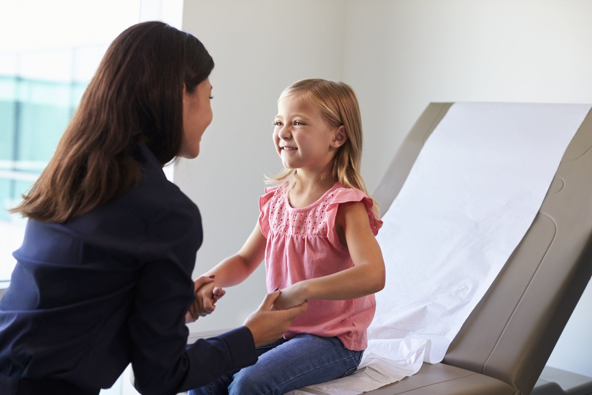 A little girl is sitting on an exam table talking to a doctor.
