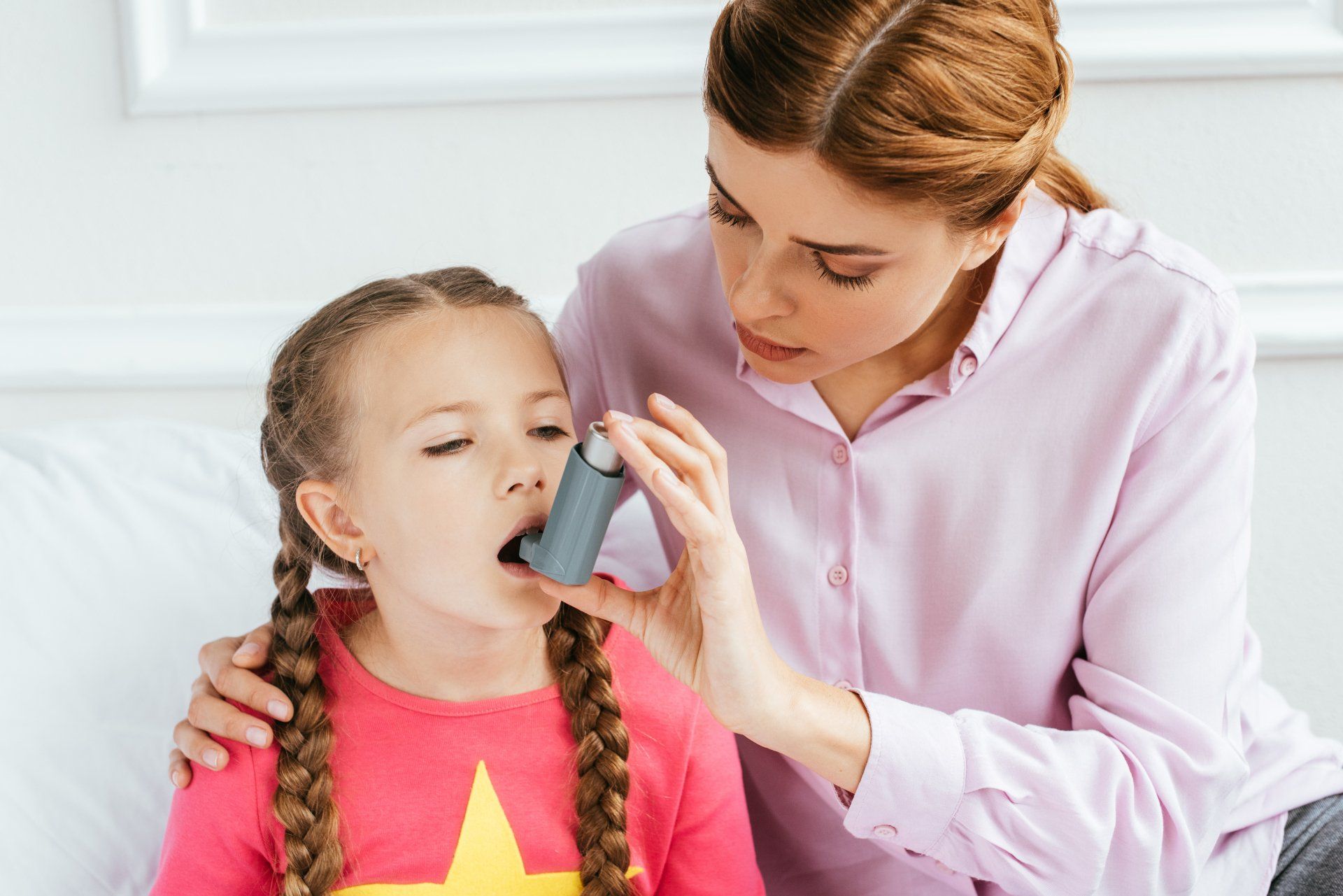A woman is helping a little girl with an inhaler.