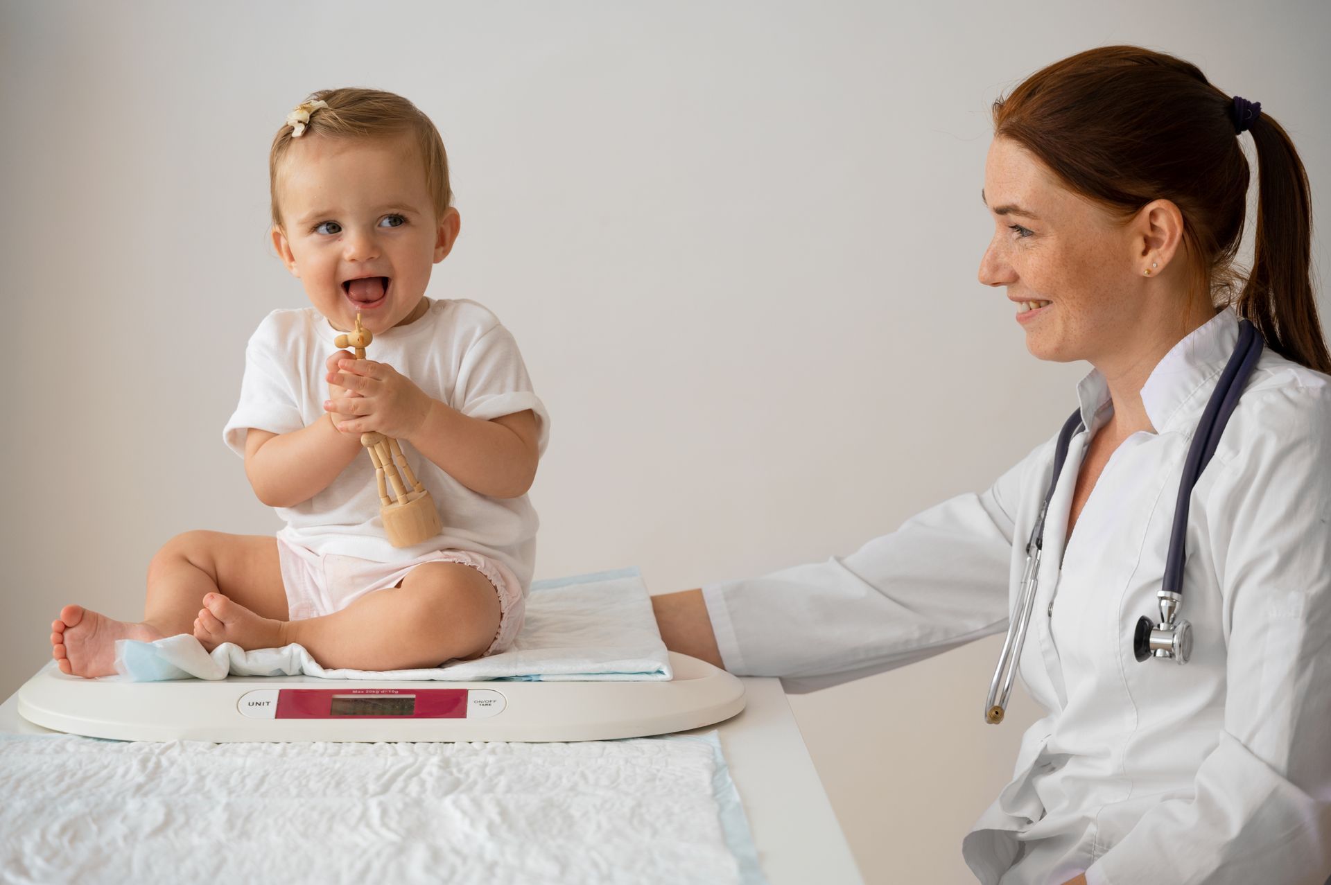 A baby is sitting on a scale next to a doctor.