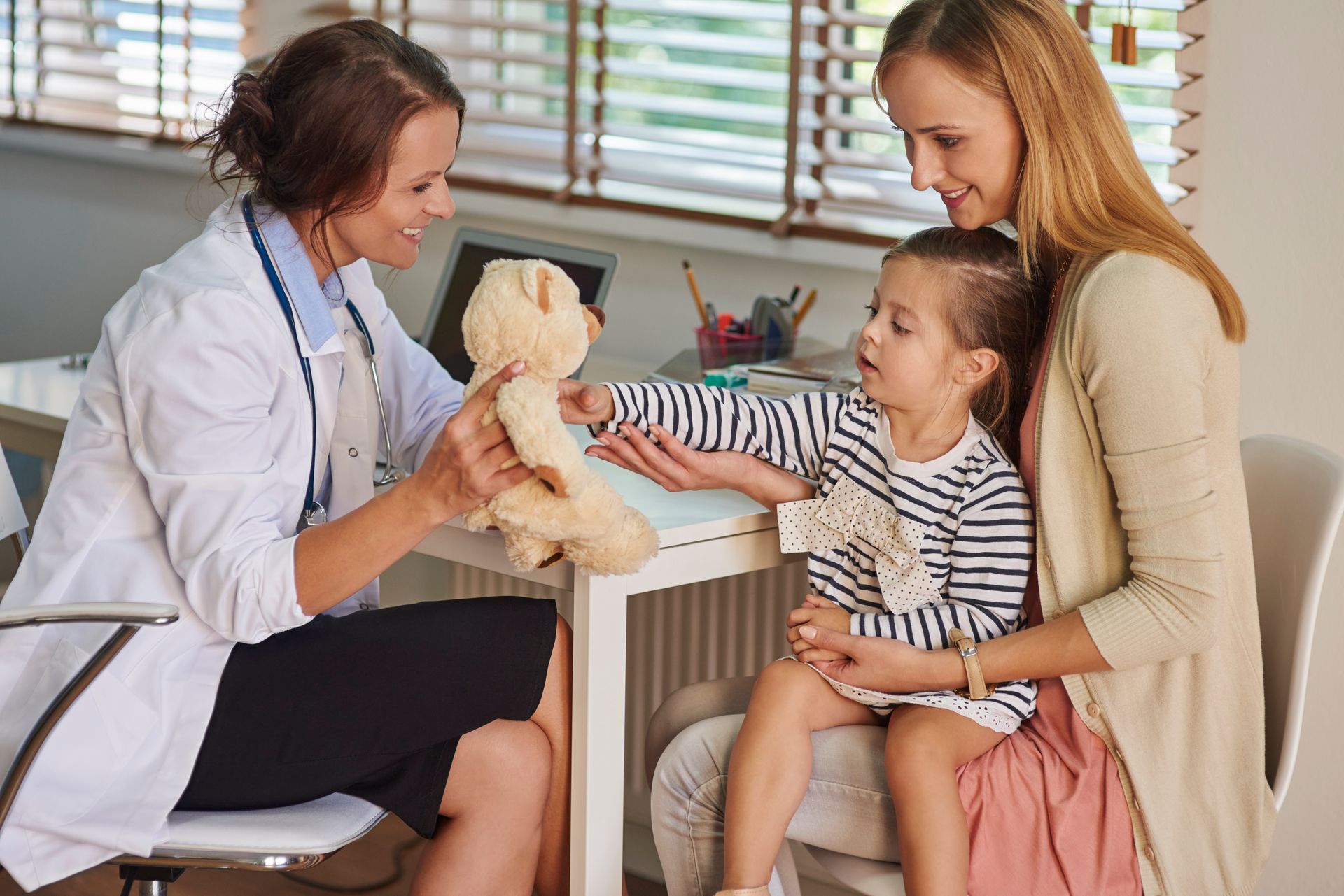 A doctor is giving a teddy bear to a little girl.