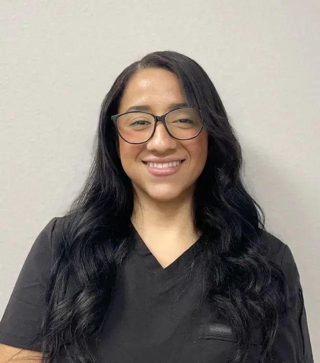 A woman wearing glasses and a black scrub top is smiling for the camera.