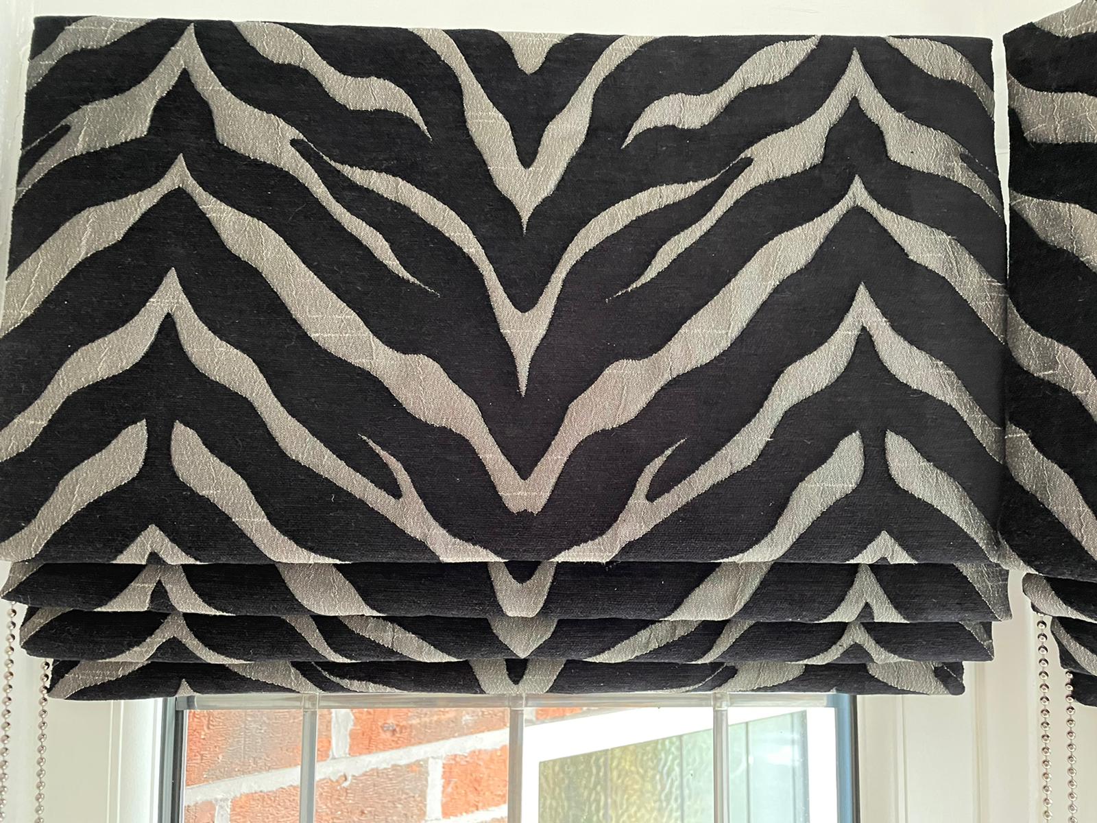 A black and white zebra print roman shade is hanging over a window.