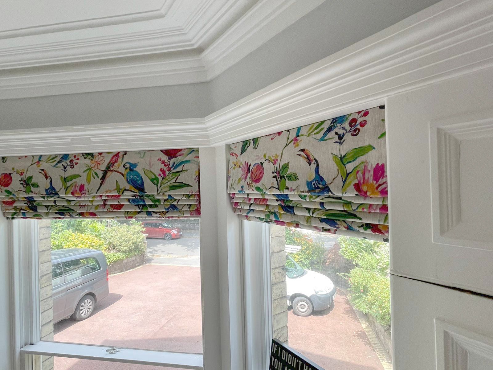 A car is parked in a driveway in front of a window with roman shades.