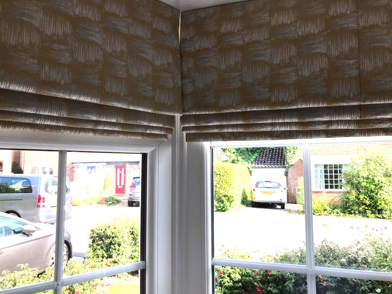 A window with roman blinds on it and a car parked in front of it.