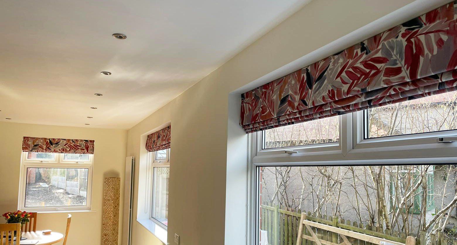 A living room with a table and chairs and a window with roman shades.
