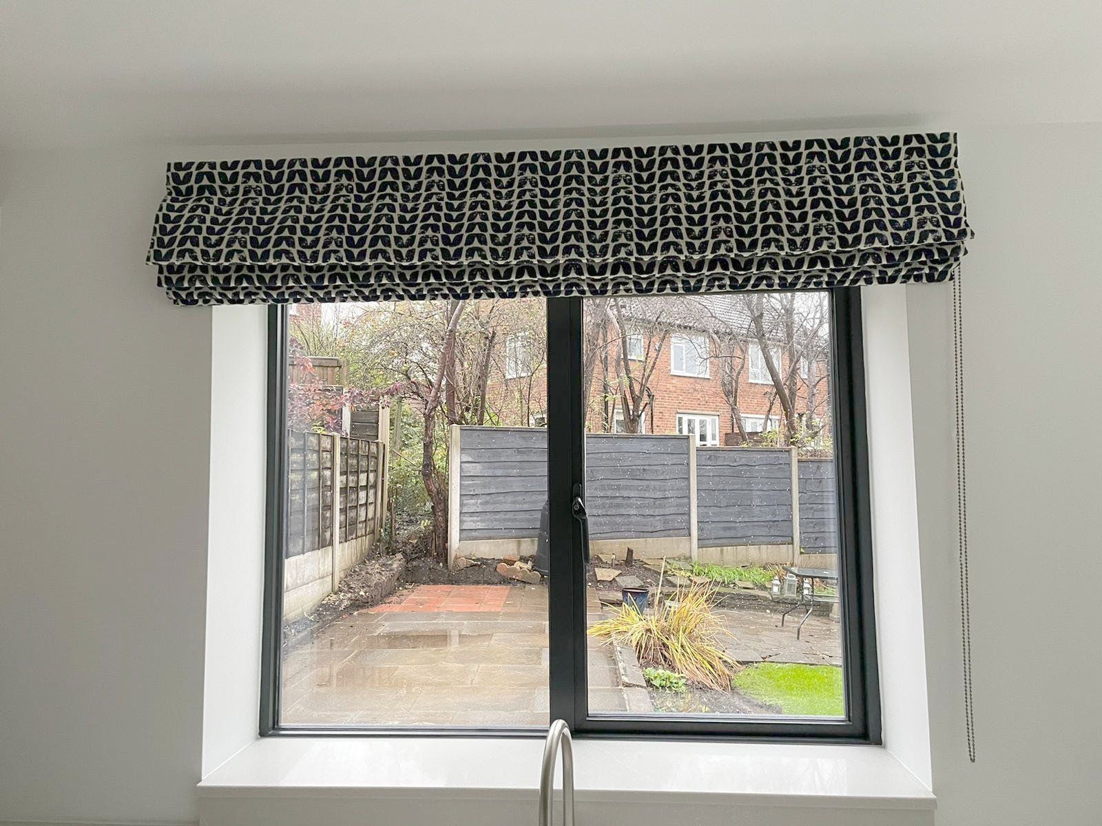A kitchen window with a black frame and a black and white roman shade.