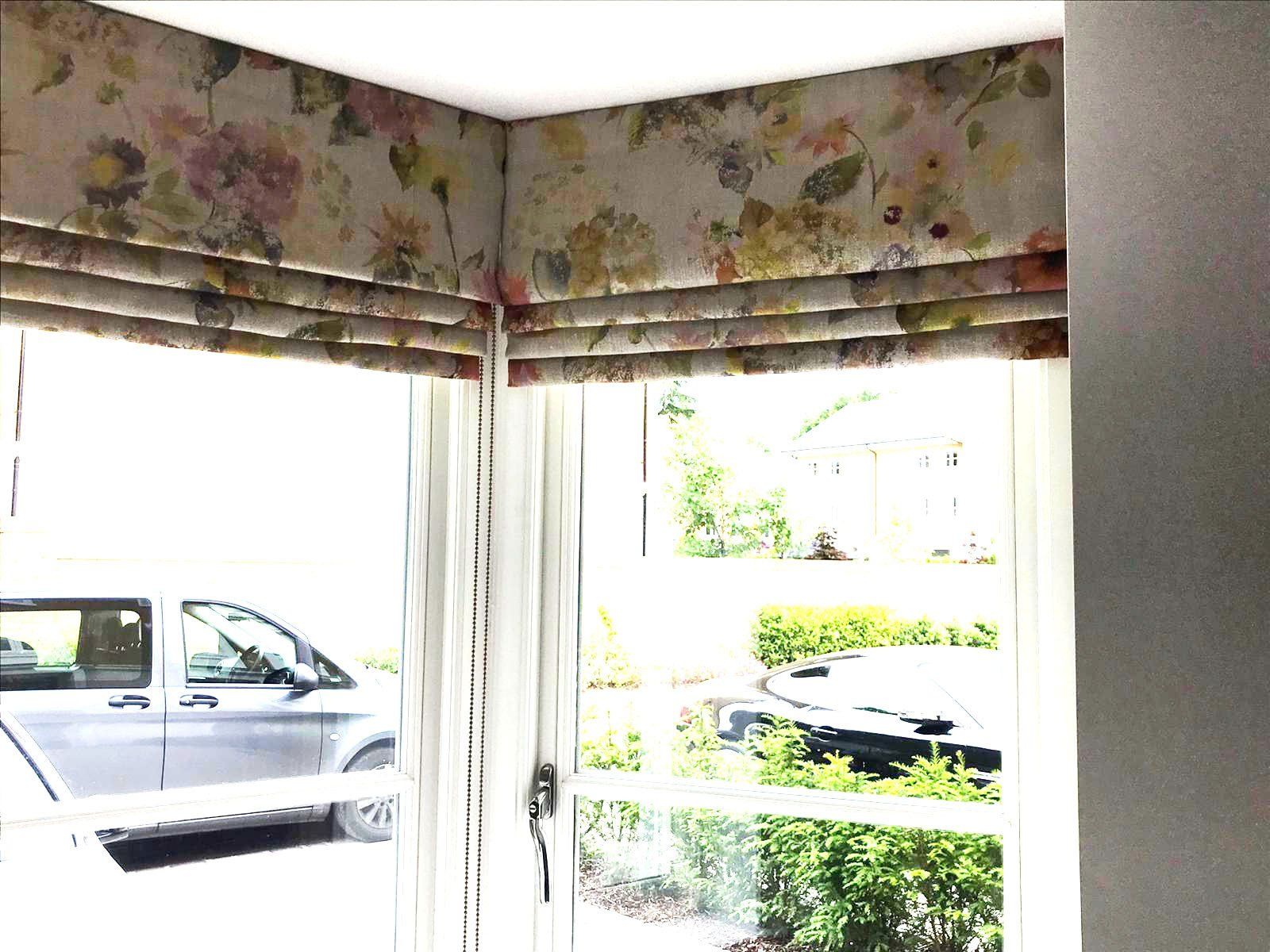 A window with a floral blind on it and a car parked in the background.