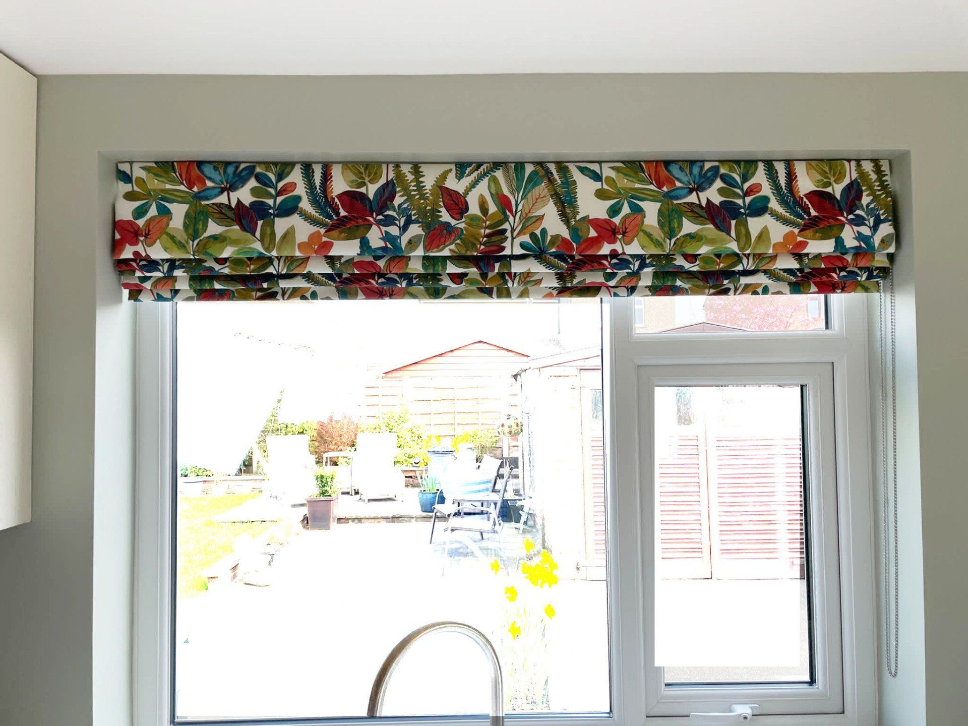 A kitchen window with a colorful roman shade and a sink.