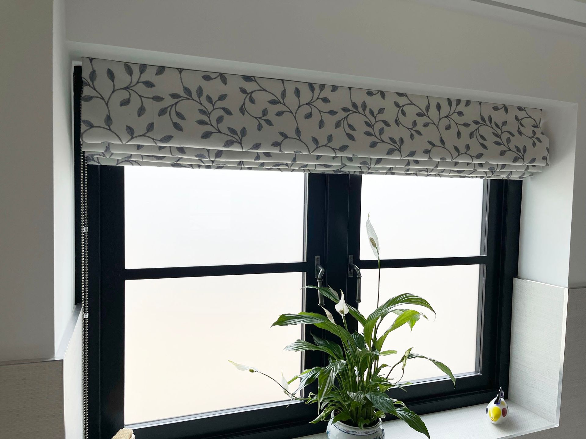 A potted plant is sitting on a window sill next to a window with a roman shade.