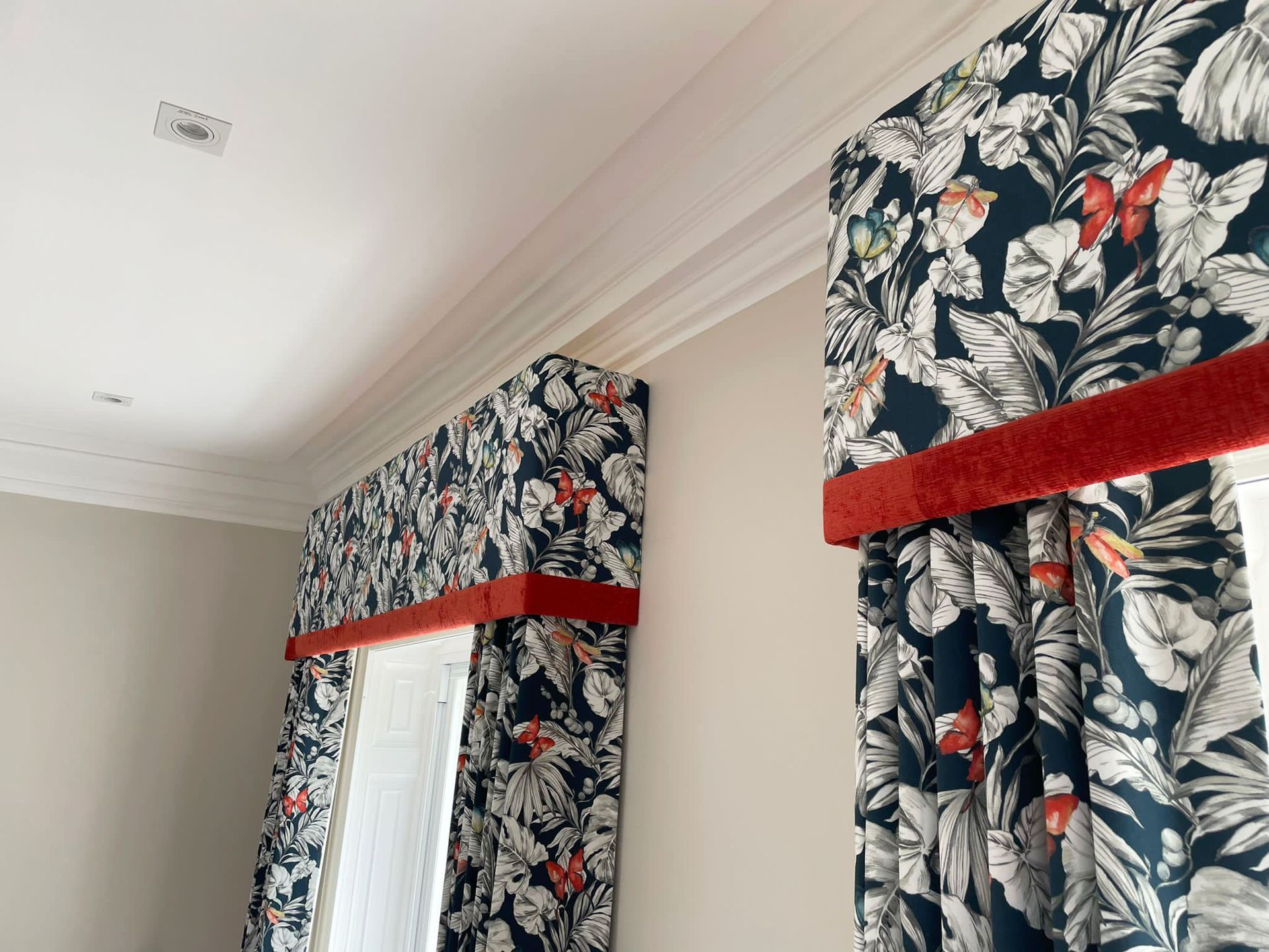 A pair of curtains with a pelmet with a red trim are hanging on a window in a room.