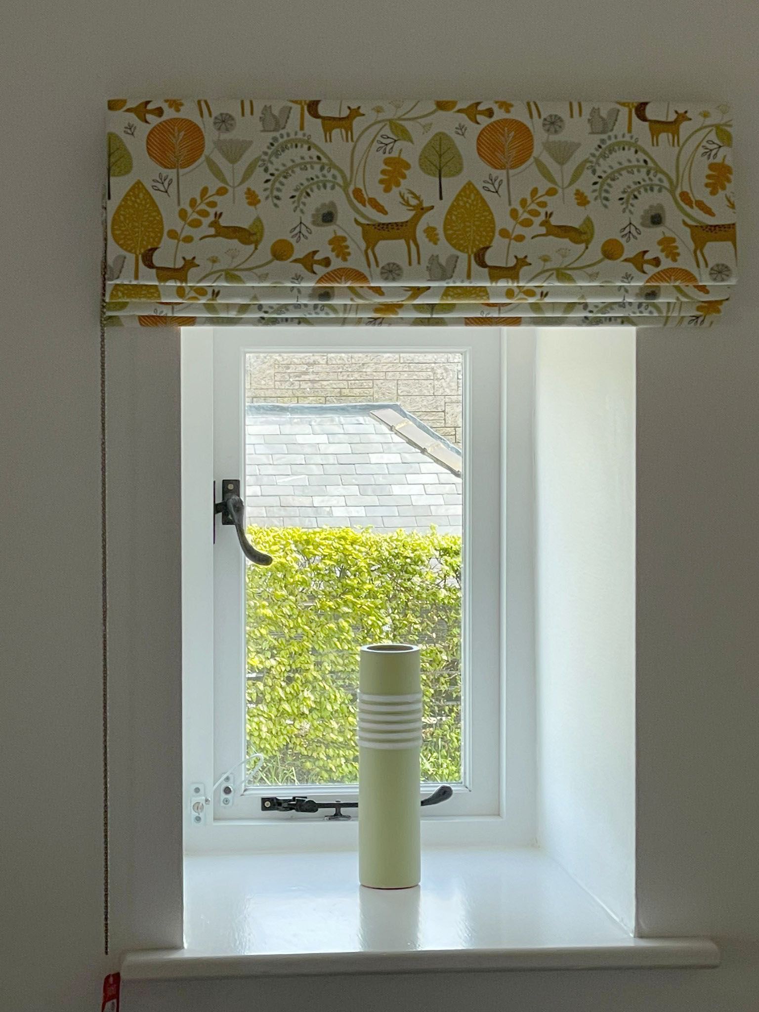 A window with a roman shade and a vase on the window sill.