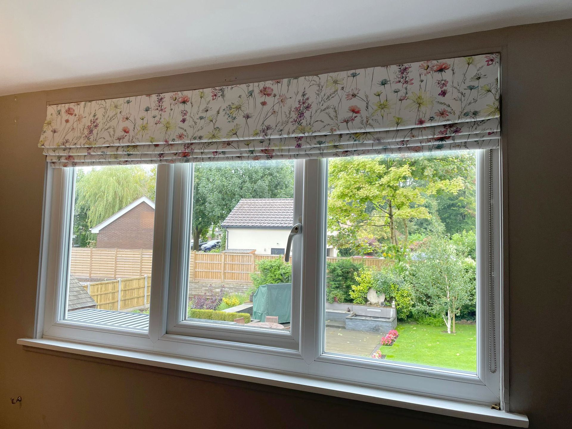 A window with a roman shade on it and a view of a garden.