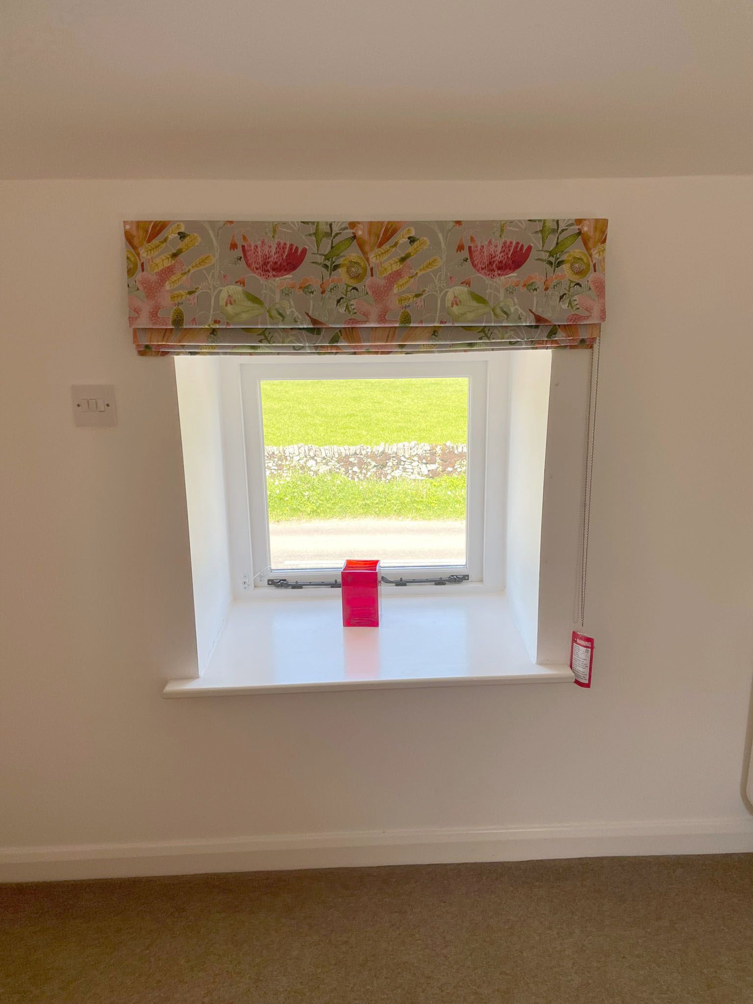 A window with a floral blind and a pink candle on the window sill.