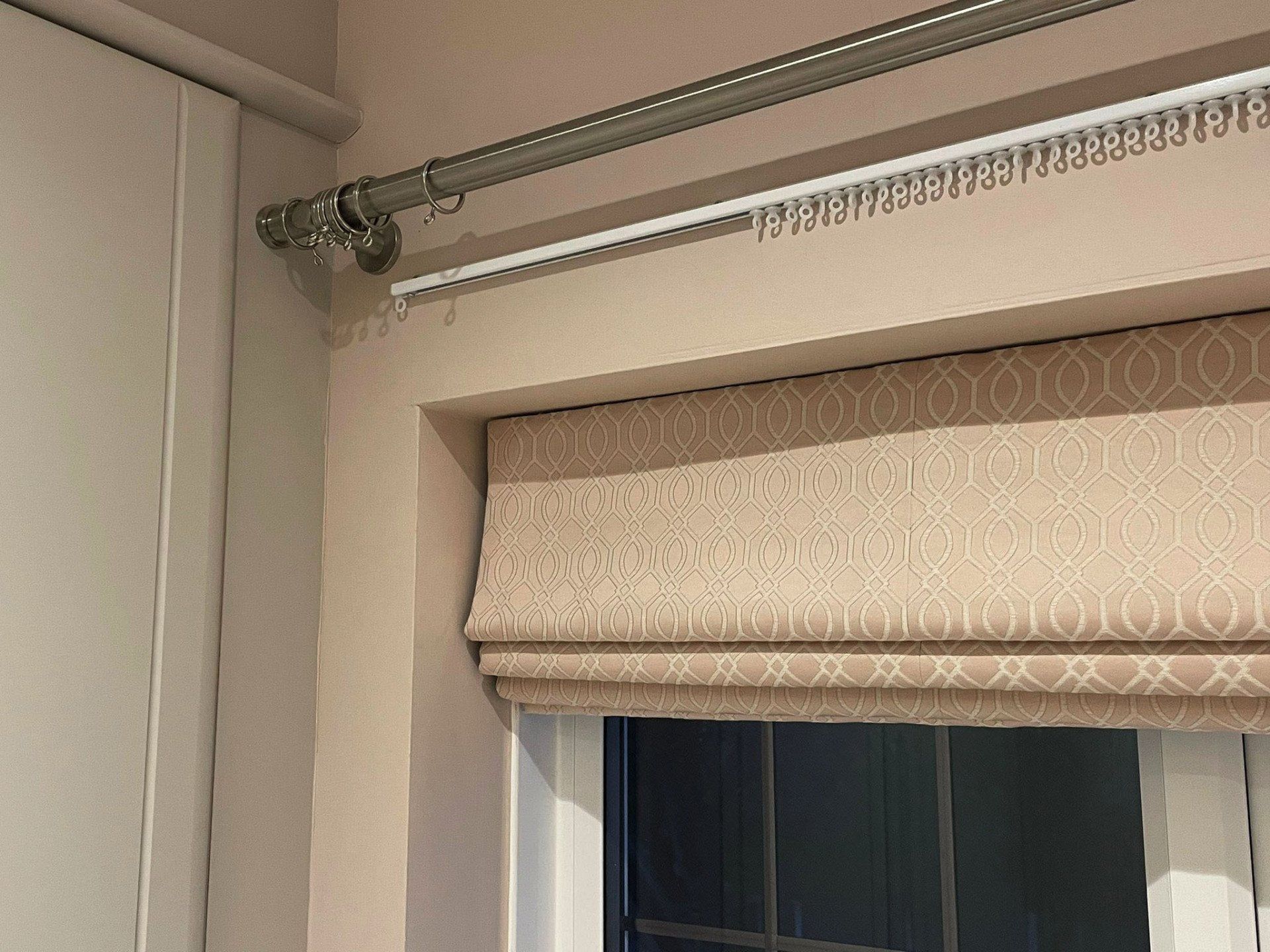 A window with a roman shade and a curtain rod.