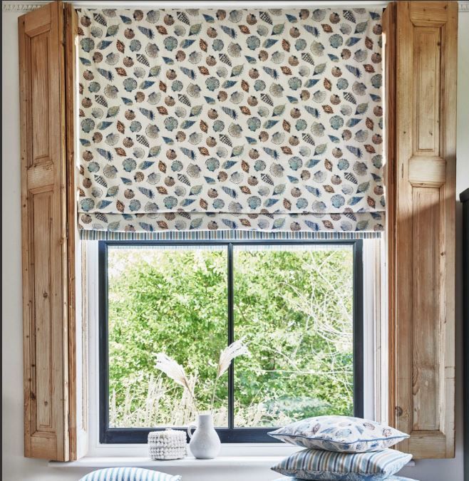 A window with a roman shade and wooden shutters