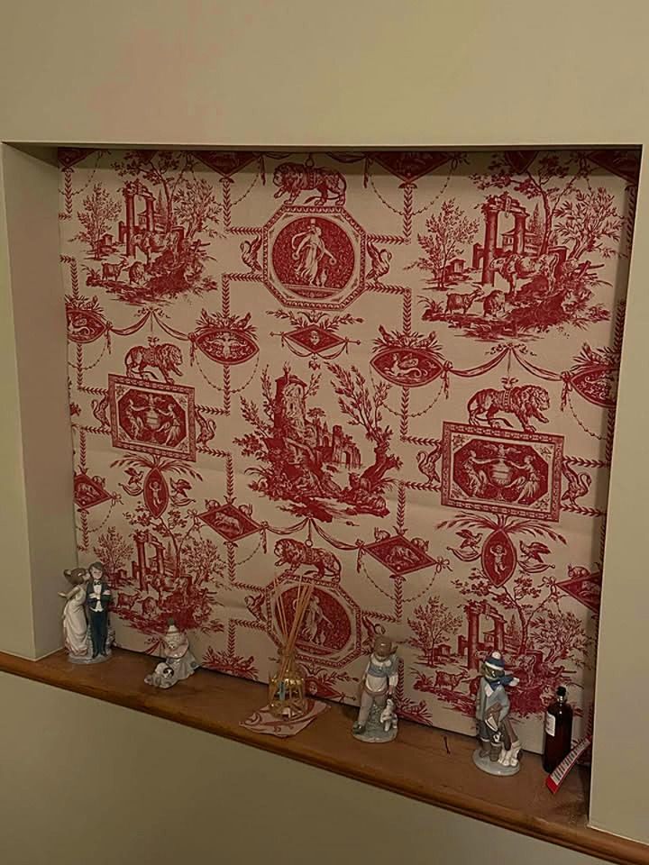 A niche in a wall with a red and white toile de jouy wallpaper.