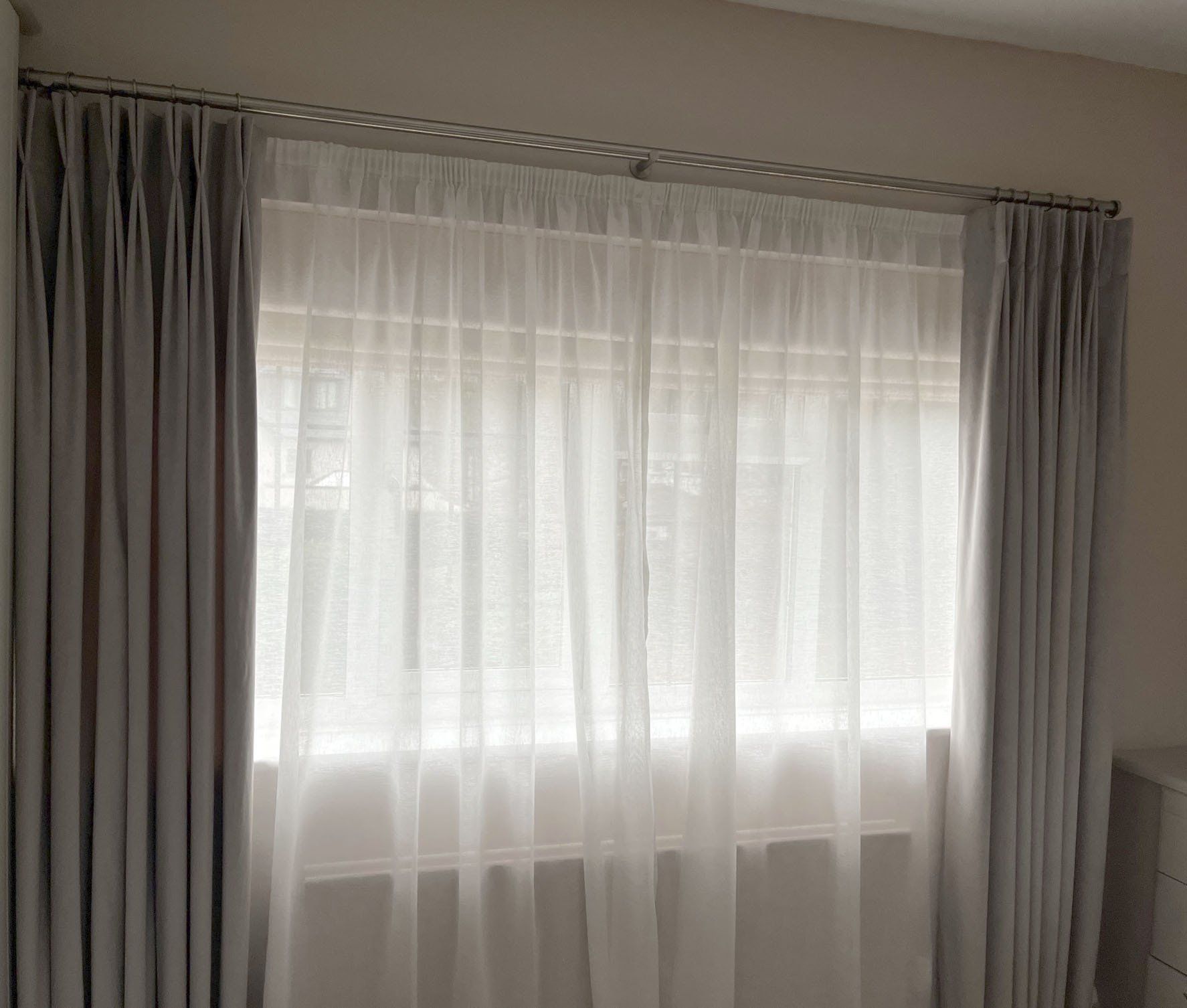 A bedroom with a large window and white curtains.