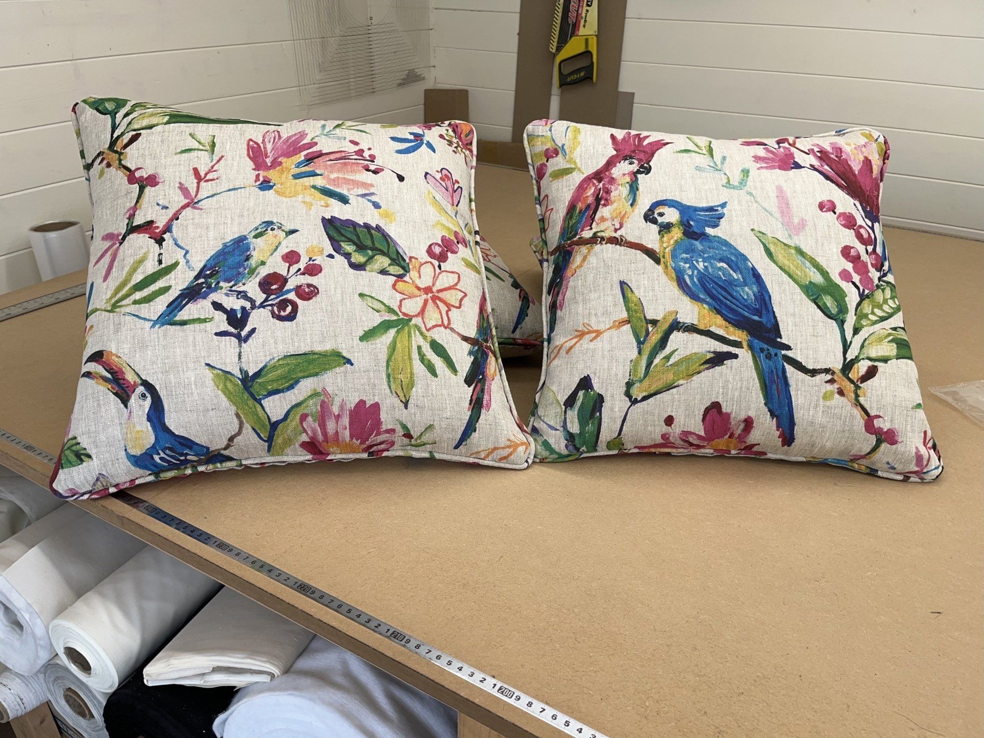 Two pillows with birds and flowers on them are sitting on a wooden table.