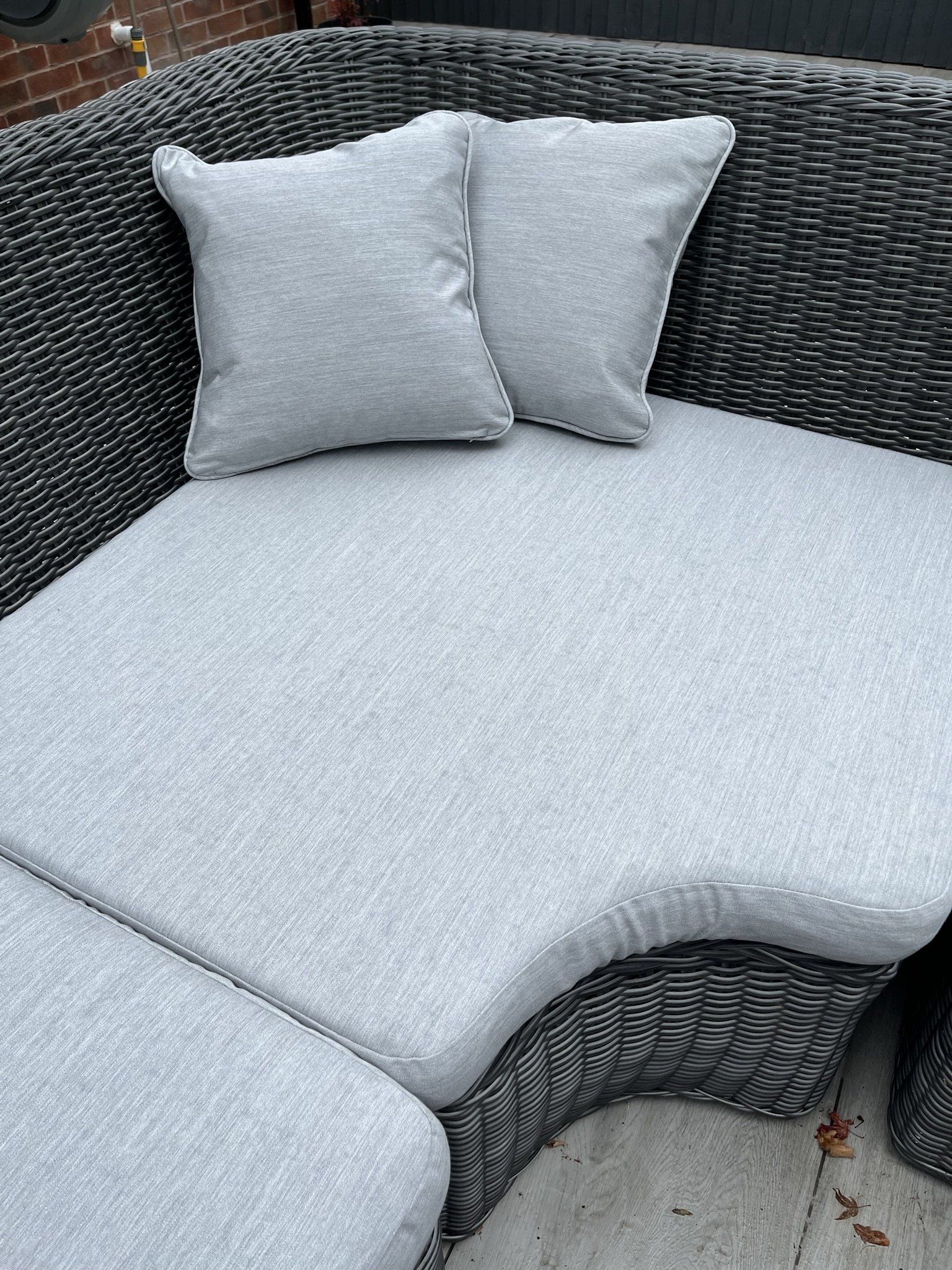 A wicker couch with two pillows on it is sitting on the ground.