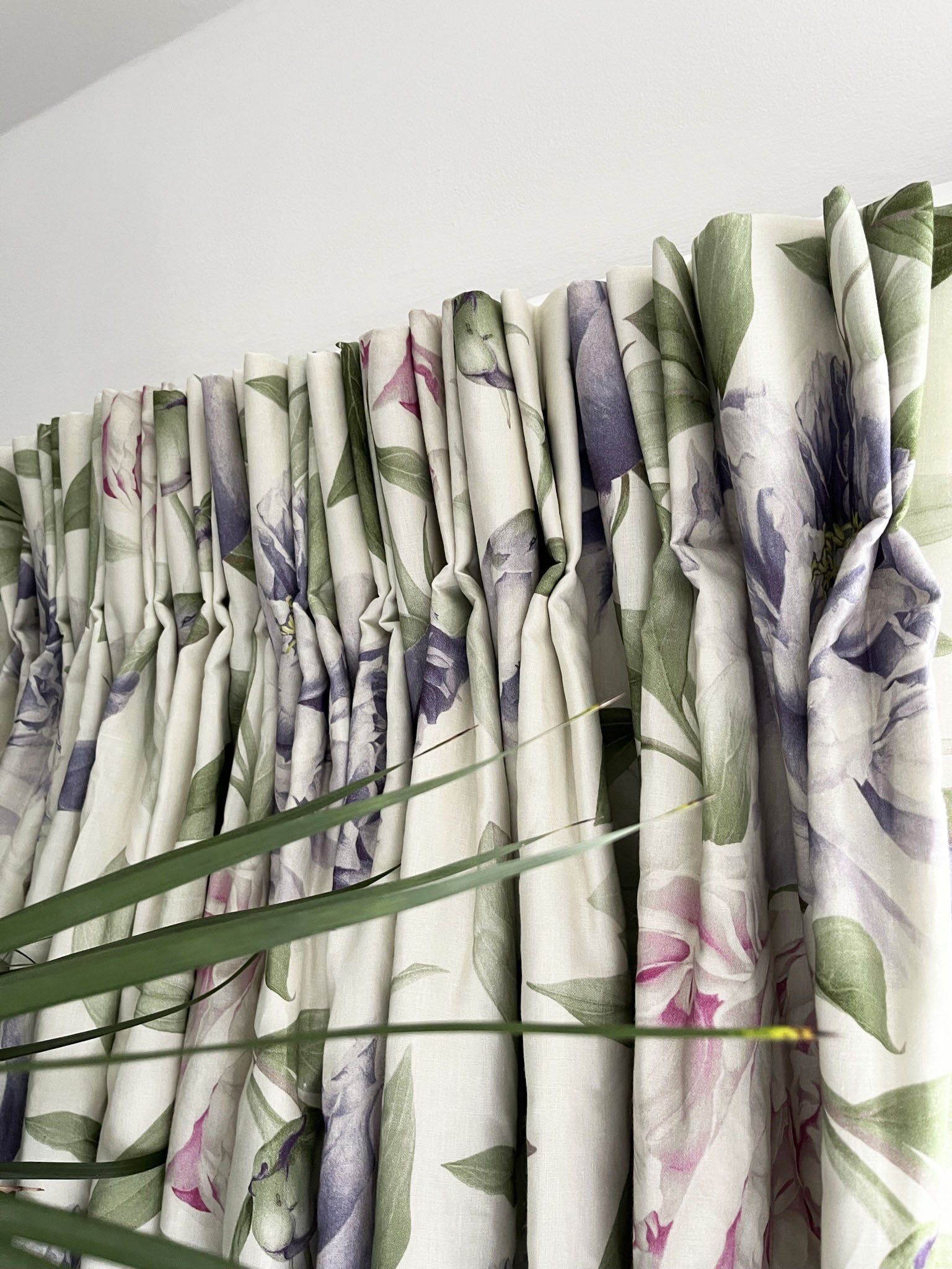 A close up of a pair of curtains with a floral pattern hanging on a window.